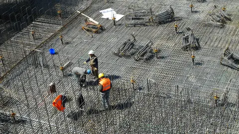 Workers tie rebar across a foundation mat before a concrete pour, the moment a permit becomes a housing start.