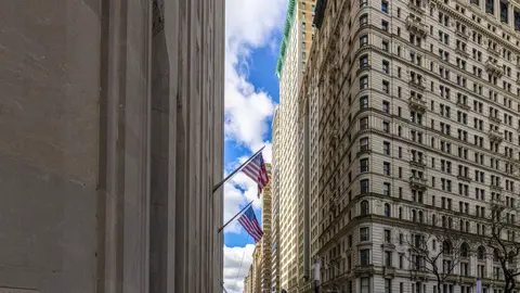 Dense urban commercial building facades along a Lower Manhattan street canyon, representing the concentration of commercial real estate assets in coastal markets facing escalating climate overlay risk designations.