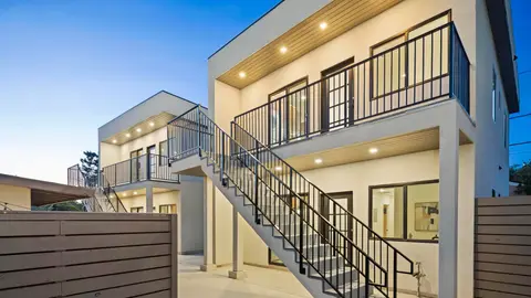 Modern two-story multifamily building with exterior staircase, balconies, and wood privacy fencing at twilight.