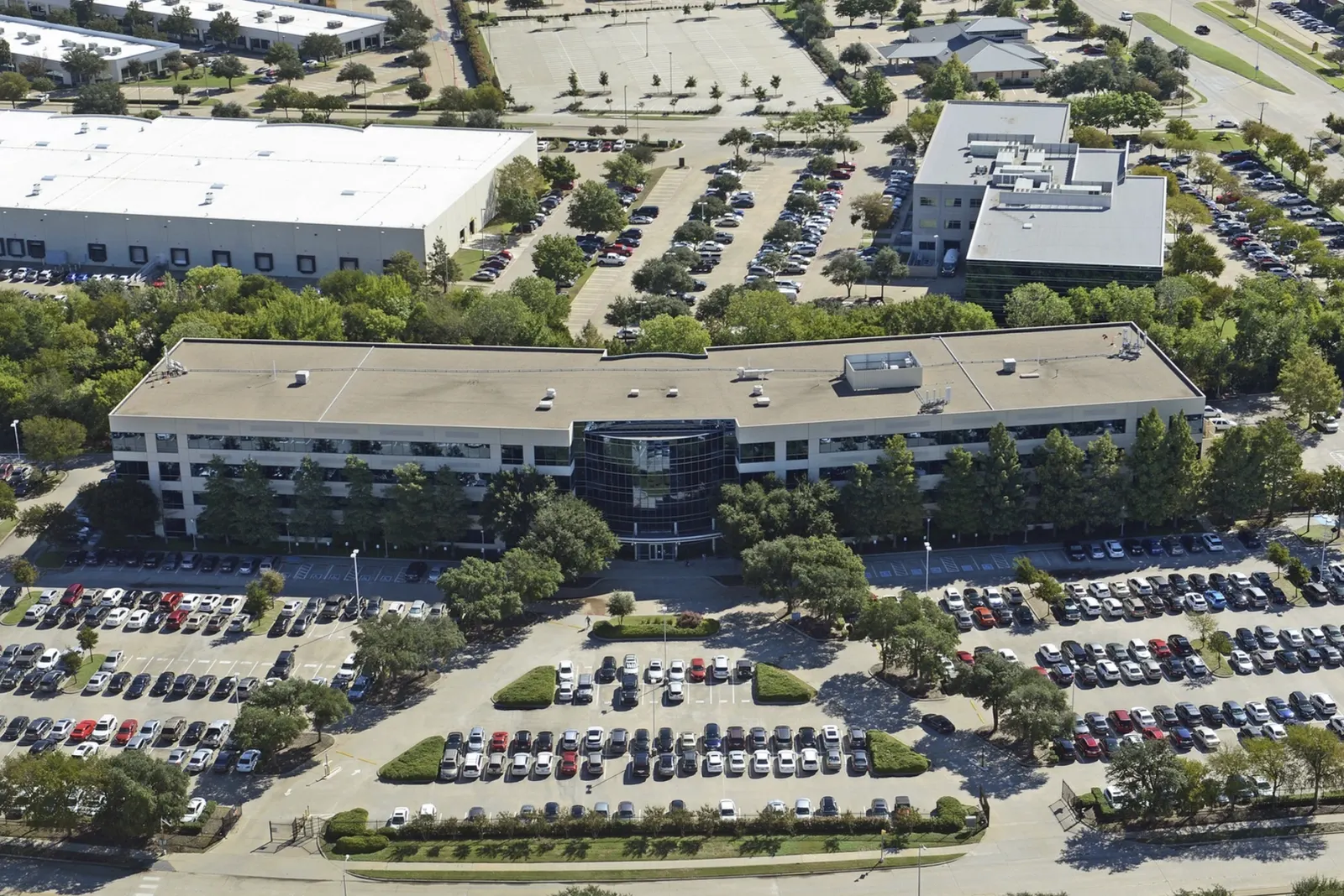 Aerial view of a suburban office campus surrounded by surface parking lots illustrating commercial parking ratio requirements and site coverage patterns.