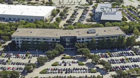 Aerial view of a suburban office campus surrounded by surface parking lots illustrating commercial parking ratio requirements and site coverage patterns.