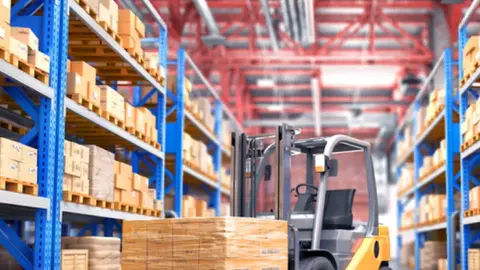 Modern warehouse with forklift moving pallets among tall storage racks.