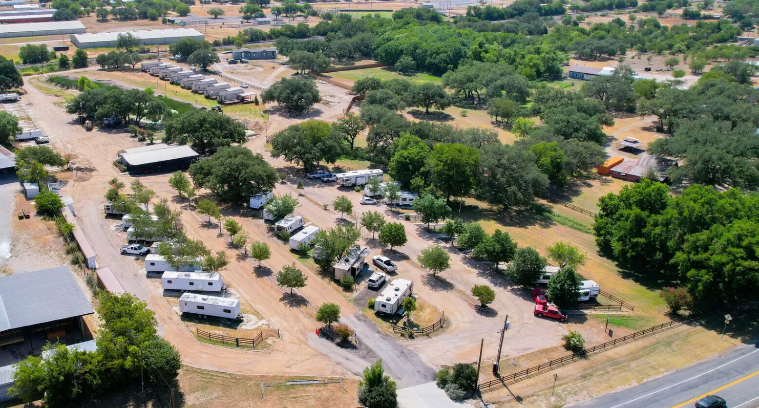Aerial view of a Texas RV park showing gravel pads, mature oak trees, and dirt road circulation, illustrating low-density site layout and rural development standards.