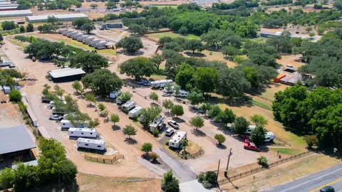 Aerial view of a Texas RV park showing gravel pads, mature oak trees, and dirt road circulation, illustrating low-density site layout and rural development standards.