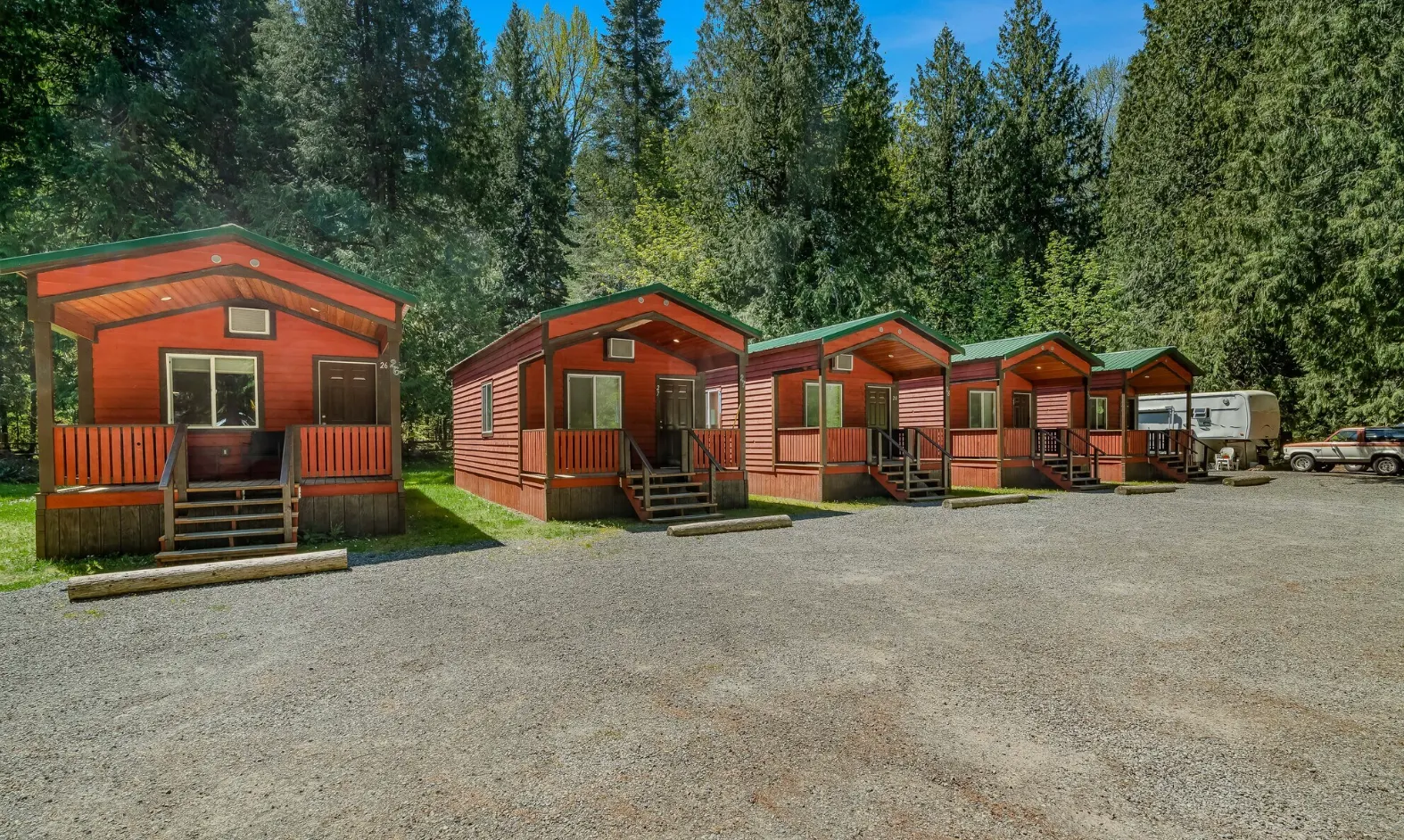 Row of modern red cabins with green roofs at a forest campground designed for remote workers, featuring high-speed Wi-Fi and comfortable work-stay accommodations surrounded by trees, an example of tech-savvy, digital-nomad-friendly campground architecture.