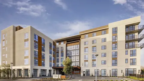 A five-story contemporary multifamily housing development featuring cream stucco and corten steel accent panels, representative of the higher-density residential infill projects emerging from accessory dwelling unit legislation and single-family zoning preemption reform across the United States.