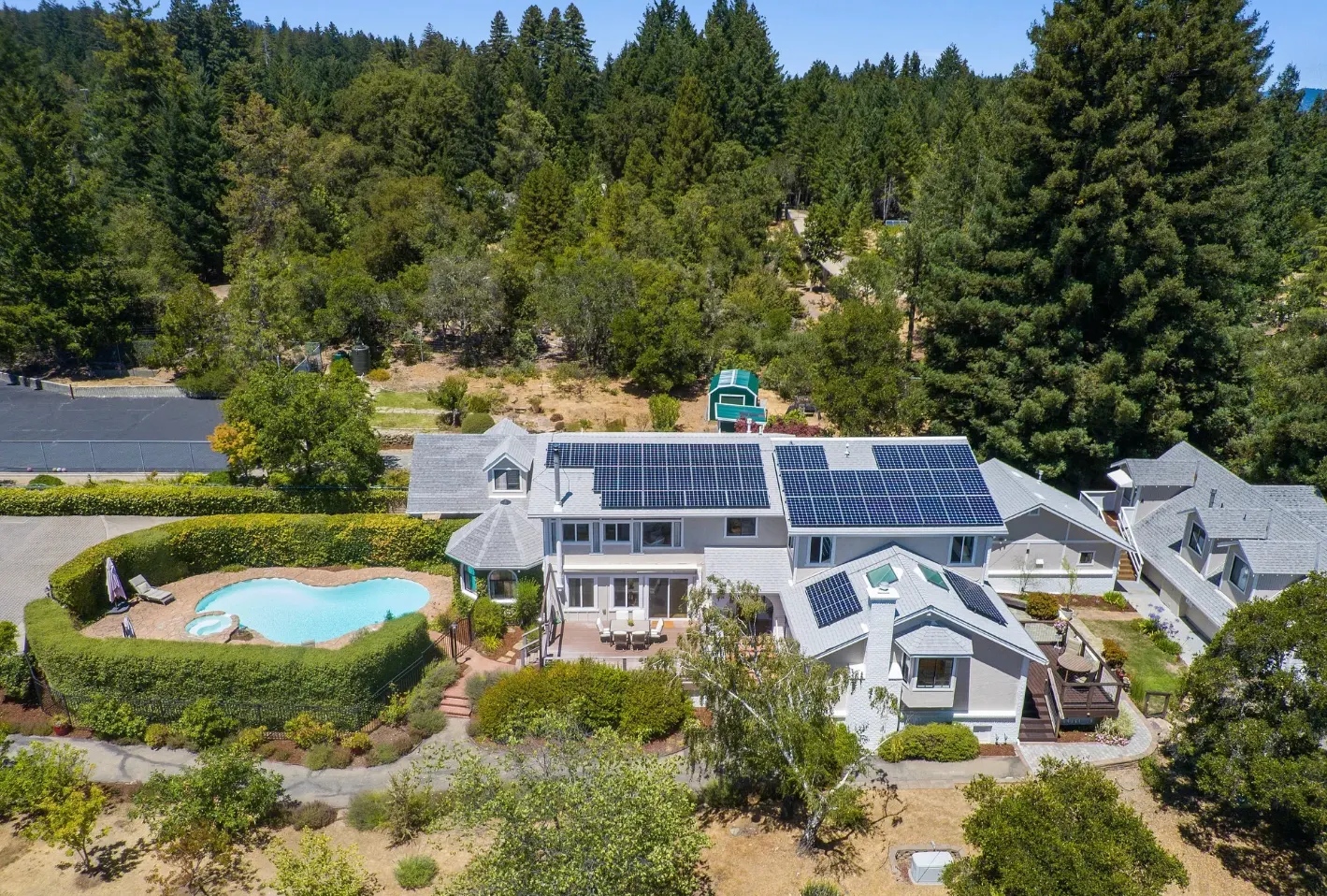 Aerial view of an entitled RV resort clubhouse with solar panels, pool, and landscaped amenities surrounded by forested land, illustrating resort-quality outdoor hospitality development.