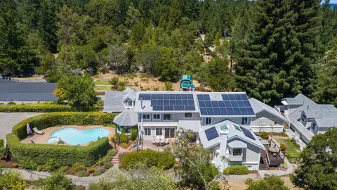 Aerial view of an entitled RV resort clubhouse with solar panels, pool, and landscaped amenities surrounded by forested land, illustrating resort-quality outdoor hospitality development.