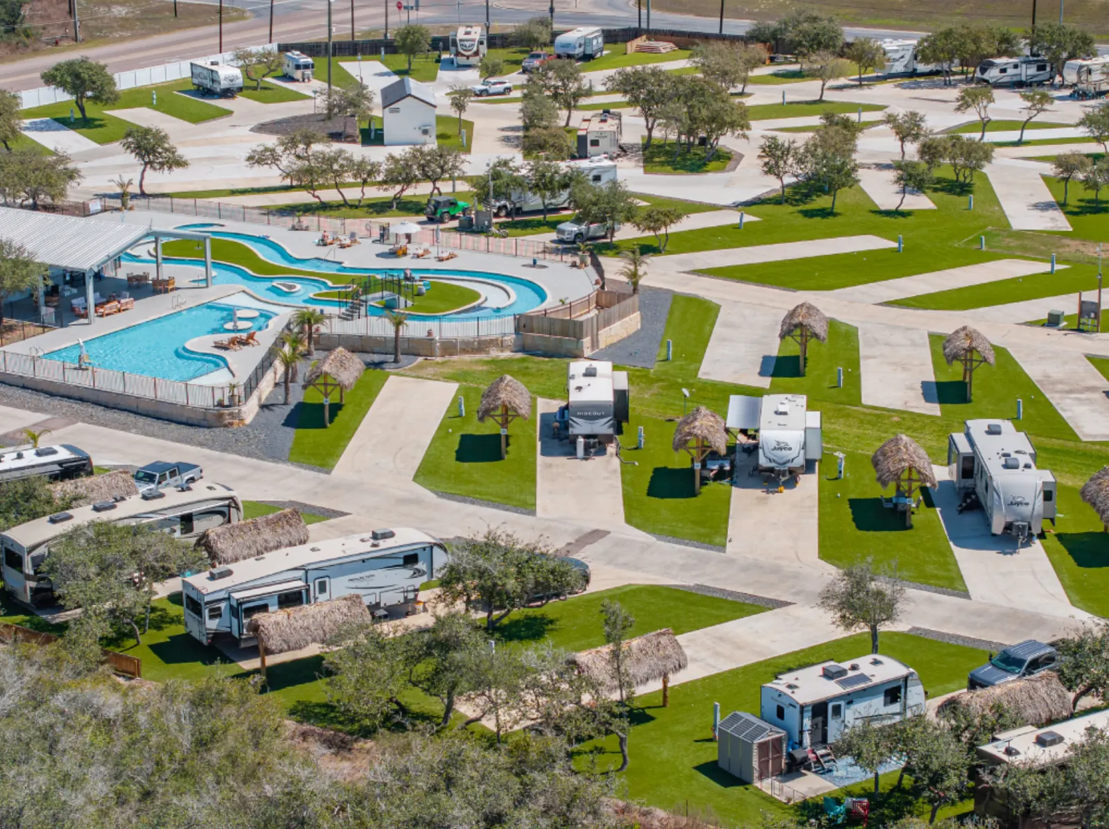 Aerial view of an RV park with concrete pads, palm-thatched shade structures and a resort-style pool