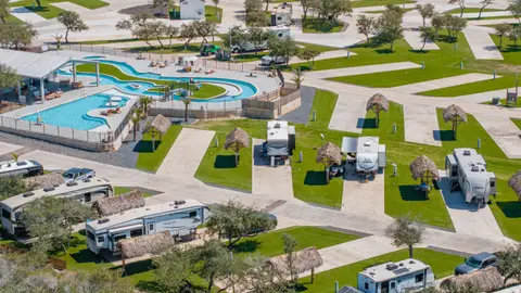 Aerial view of an RV park with concrete pads, palm-thatched shade structures and a resort-style pool