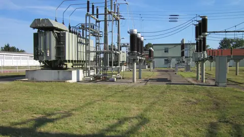 An electrical substation with transformers and steel gantries sitting in open grass, well back from the property edge.